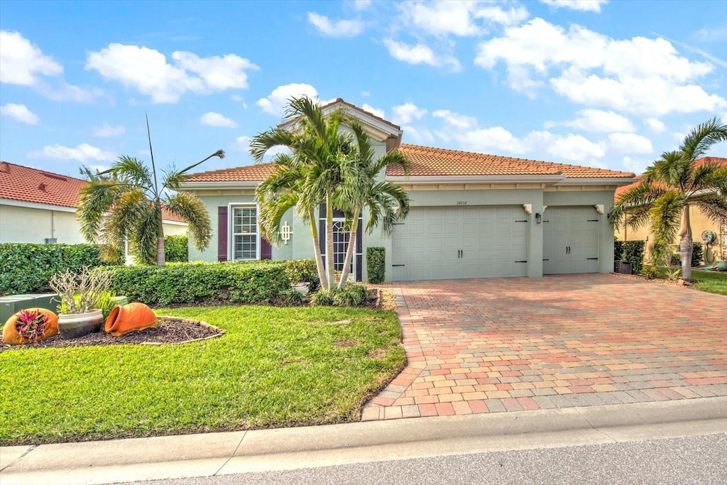 mediterranean / spanish house featuring a garage, a tile roof, decorative driveway, stucco siding, and a front yard