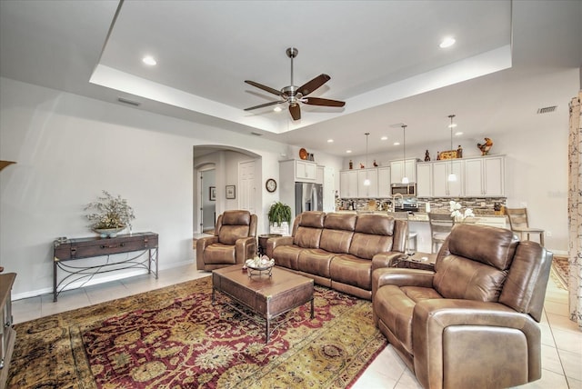 living area featuring arched walkways, a tray ceiling, visible vents, and a ceiling fan