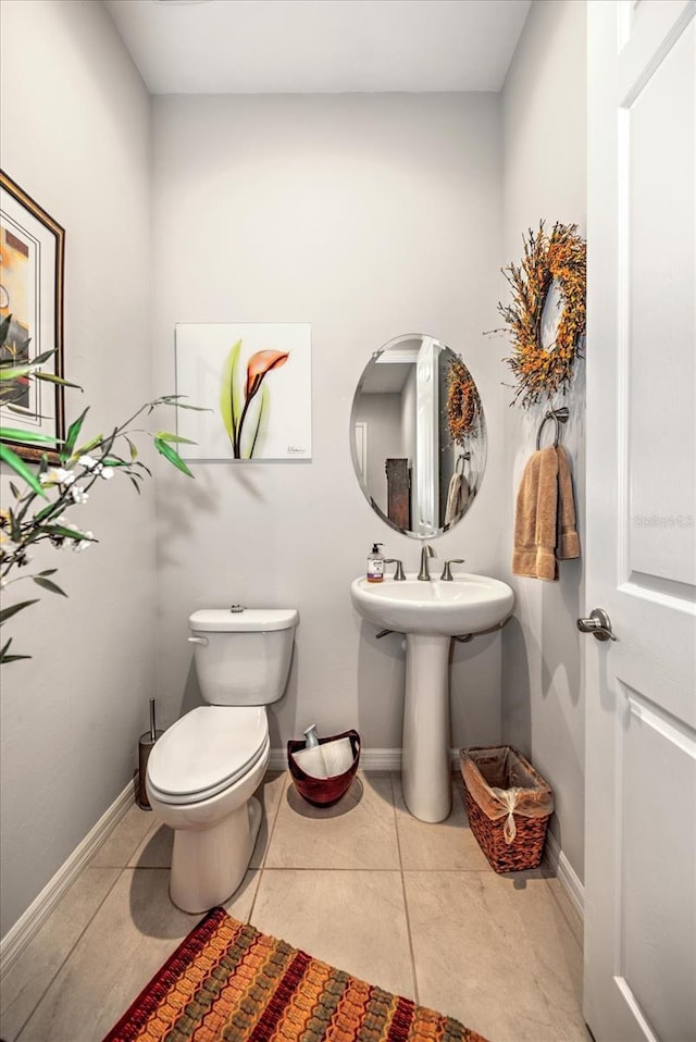 half bathroom featuring toilet, baseboards, a sink, and tile patterned floors