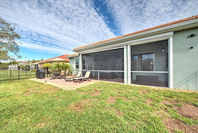 back of property featuring stucco siding, a lawn, a sunroom, a patio area, and fence