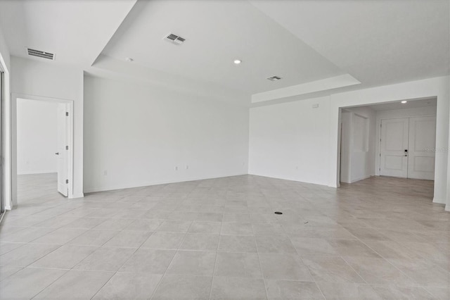 empty room with a raised ceiling, visible vents, and baseboards