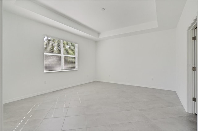 spare room featuring a tray ceiling, light tile patterned flooring, and baseboards