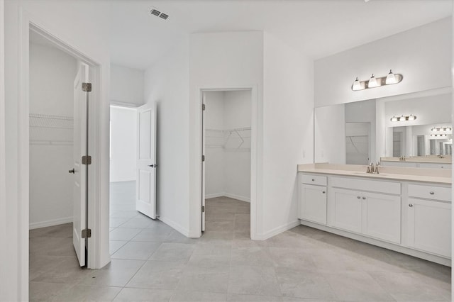 bathroom featuring baseboards, visible vents, tile patterned floors, a walk in closet, and vanity