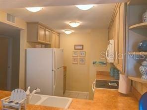 kitchen with stove, a sink, visible vents, freestanding refrigerator, and open shelves