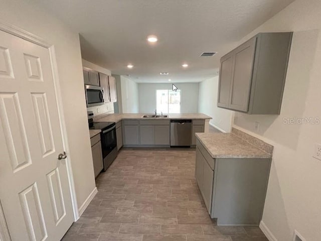 kitchen with stainless steel appliances, a peninsula, visible vents, and gray cabinetry