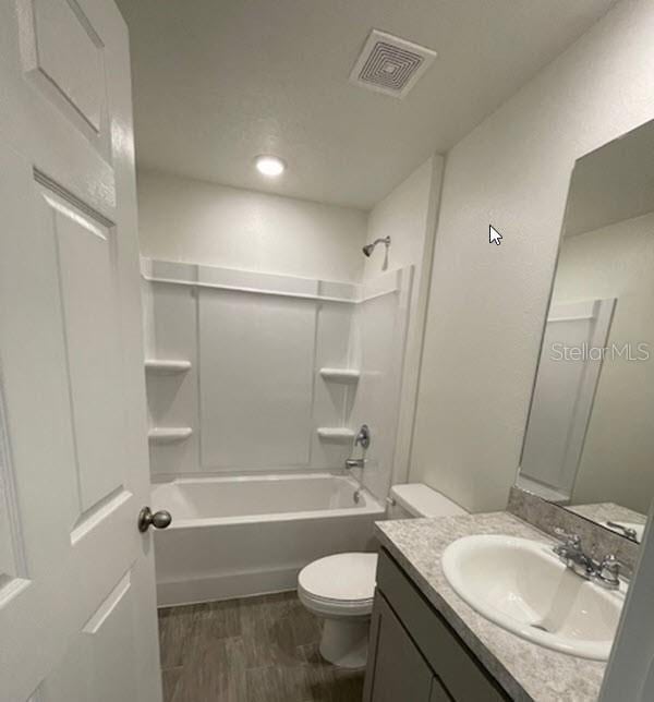 full bathroom with visible vents, toilet, vanity, wood finished floors, and shower / bathtub combination