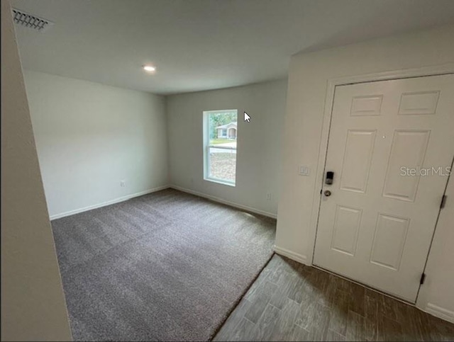 entrance foyer with carpet floors, baseboards, visible vents, and wood finished floors