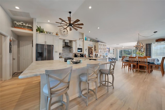 kitchen featuring white cabinets, a kitchen breakfast bar, a center island, stainless steel appliances, and wall chimney range hood