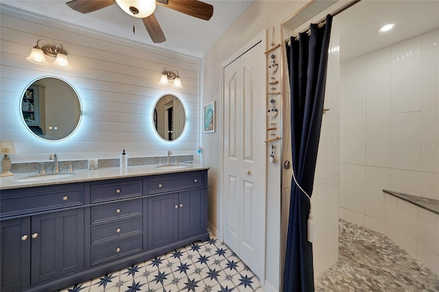 full bathroom with a ceiling fan, a sink, a tile shower, and double vanity