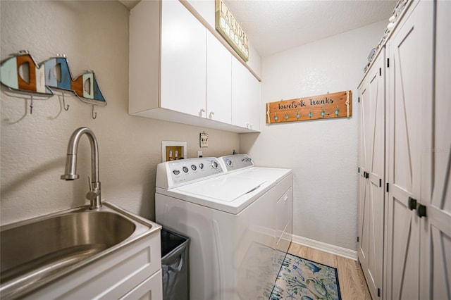 clothes washing area with washer and clothes dryer, cabinet space, light wood-style flooring, a sink, and a textured ceiling