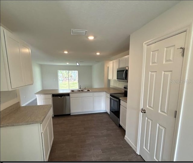 kitchen featuring dark wood-style floors, appliances with stainless steel finishes, white cabinets, a sink, and a peninsula