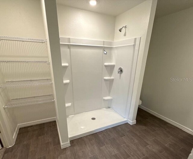 bathroom featuring a stall shower, baseboards, toilet, and wood finished floors