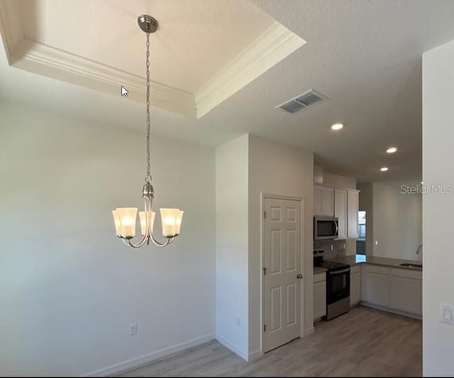 kitchen with visible vents, white cabinets, a raised ceiling, stainless steel appliances, and a sink