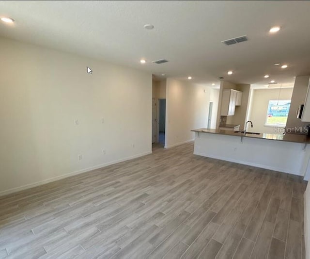 unfurnished living room with light wood-style flooring, recessed lighting, a sink, visible vents, and baseboards