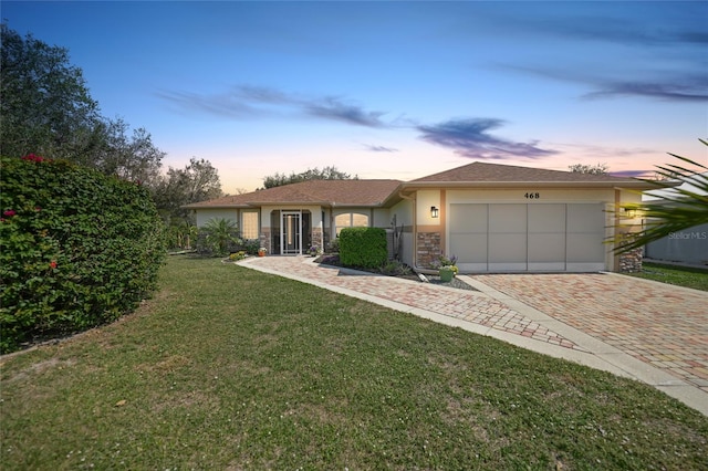 view of front facade featuring a garage, stone siding, decorative driveway, a front yard, and stucco siding