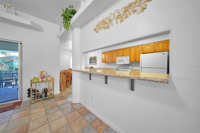 kitchen with light stone counters, a kitchen bar, visible vents, white appliances, and baseboards