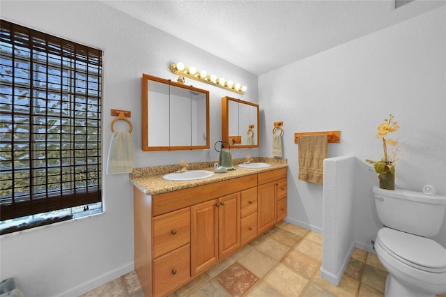 full bathroom with toilet, a textured ceiling, double vanity, and a sink