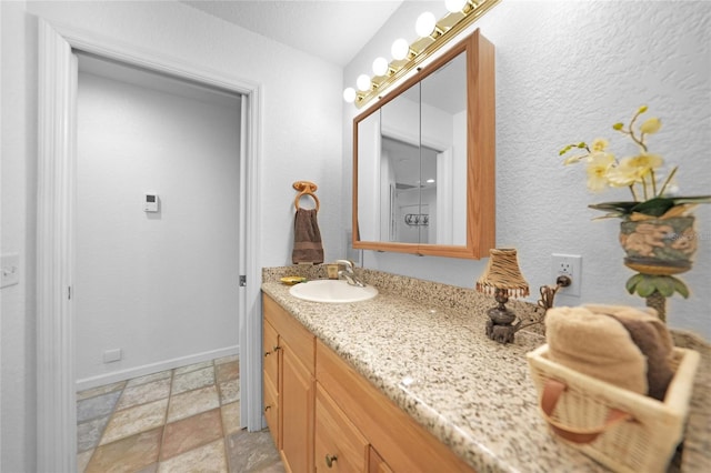 bathroom featuring baseboards, stone tile flooring, and vanity