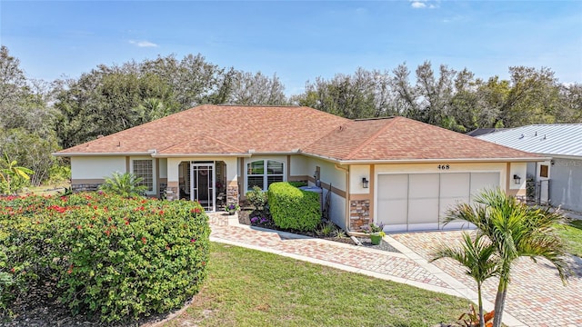 ranch-style house featuring a shingled roof, stone siding, stucco siding, an attached garage, and a front yard