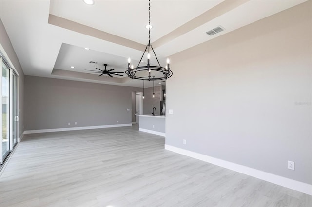 empty room featuring light wood finished floors, visible vents, baseboards, a tray ceiling, and ceiling fan with notable chandelier