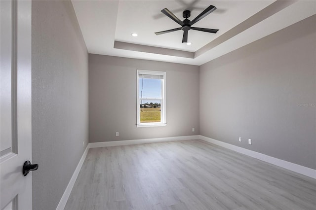 spare room with light wood finished floors, ceiling fan, a tray ceiling, and baseboards