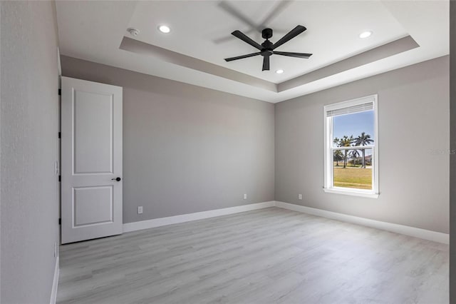 spare room with light wood-type flooring, a raised ceiling, and baseboards