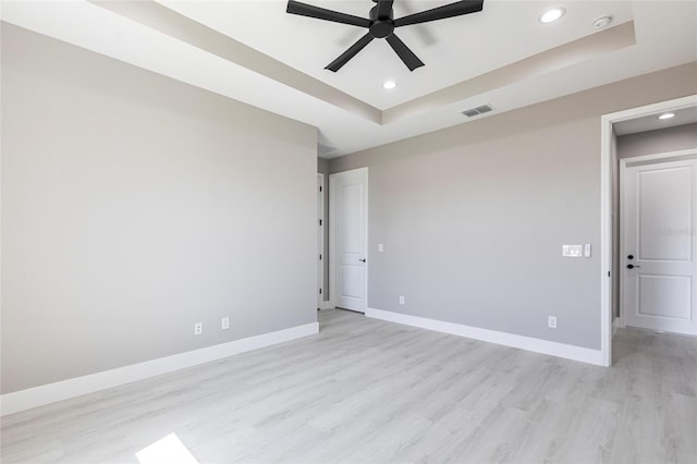 empty room featuring a tray ceiling, recessed lighting, a ceiling fan, light wood-type flooring, and baseboards