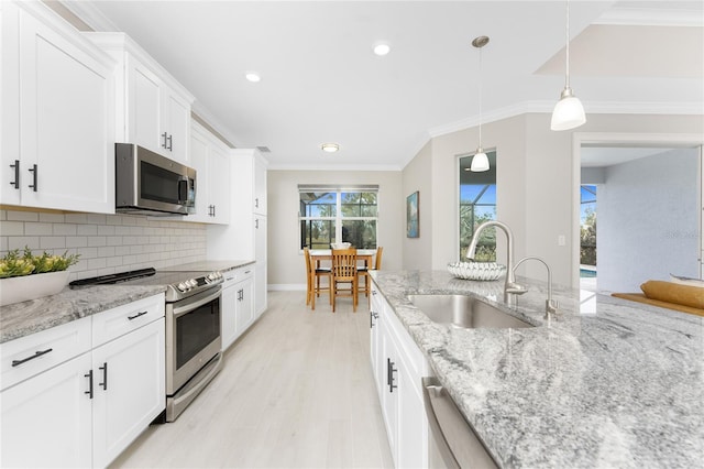 kitchen featuring ornamental molding, a sink, stainless steel appliances, light wood-type flooring, and backsplash