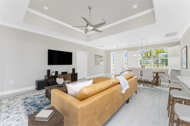 living area with a tray ceiling, light wood-style flooring, visible vents, and crown molding