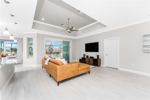 living room featuring a tray ceiling, visible vents, plenty of natural light, and light wood finished floors