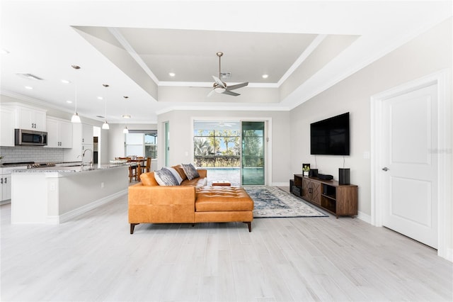 living room featuring ornamental molding, a tray ceiling, light wood finished floors, and visible vents