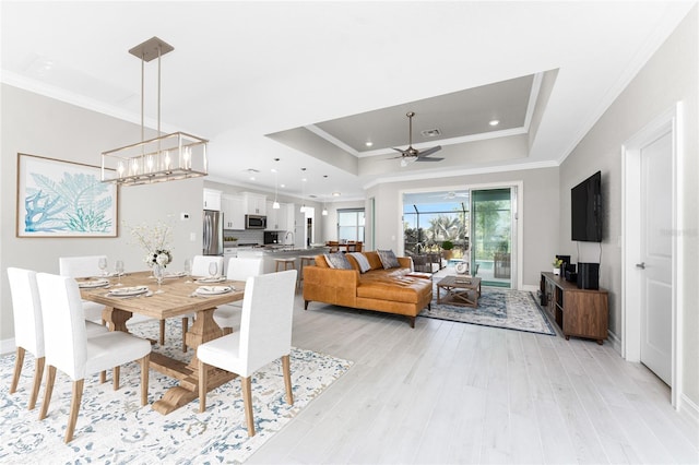 dining space with a tray ceiling, visible vents, ornamental molding, light wood-type flooring, and ceiling fan with notable chandelier