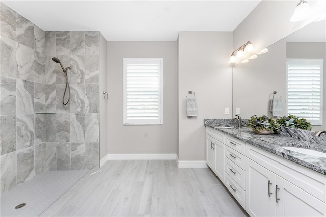 full bath with wood finished floors, a sink, baseboards, tiled shower, and double vanity