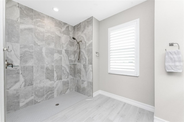 bathroom with tiled shower, wood finish floors, and baseboards