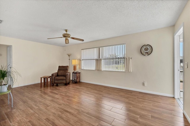 sitting room featuring ceiling fan, a textured ceiling, baseboards, and wood finished floors