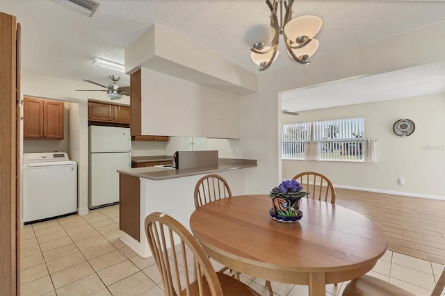 dining room with a textured ceiling, light tile patterned floors, ceiling fan with notable chandelier, baseboards, and washer / clothes dryer