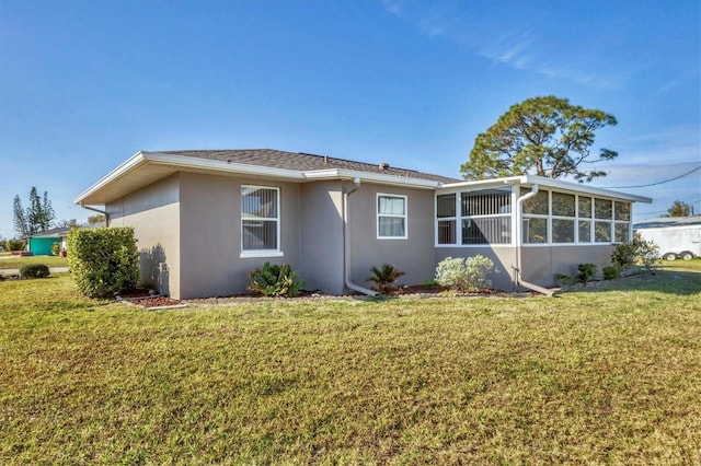 rear view of property with a sunroom, a lawn, and stucco siding