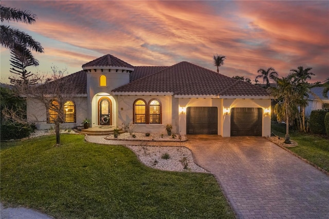 mediterranean / spanish home featuring stucco siding, a lawn, decorative driveway, an attached garage, and a tiled roof