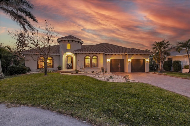 mediterranean / spanish home with an attached garage, stucco siding, a front lawn, a tiled roof, and decorative driveway