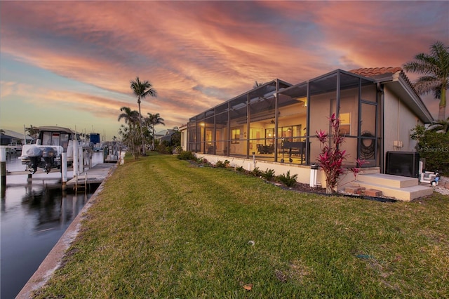 back of house at dusk with a lawn, a tile roof, glass enclosure, and a water view