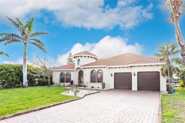 mediterranean / spanish-style home featuring a front yard, stucco siding, a garage, a tile roof, and decorative driveway