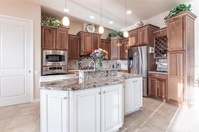 kitchen featuring tasteful backsplash, light stone countertops, decorative light fixtures, stainless steel appliances, and a kitchen island with sink