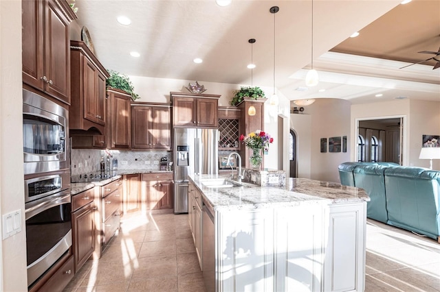 kitchen featuring light stone counters, a sink, decorative backsplash, stainless steel appliances, and open floor plan