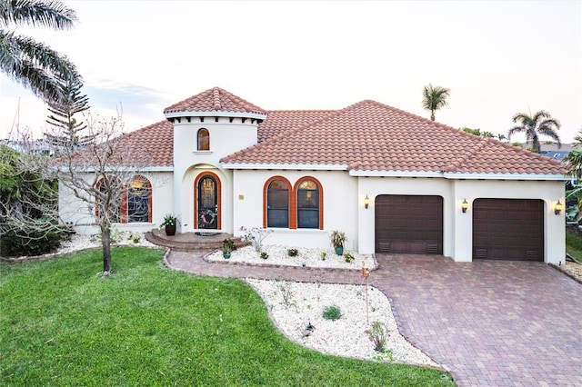 mediterranean / spanish house with a tiled roof, a front yard, stucco siding, decorative driveway, and an attached garage