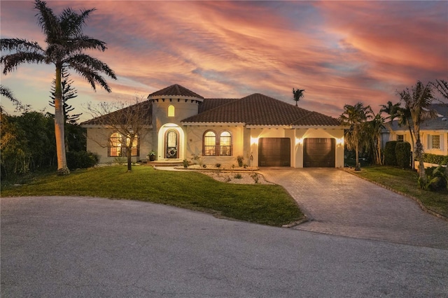 mediterranean / spanish-style house featuring a tile roof, a front yard, stucco siding, decorative driveway, and an attached garage