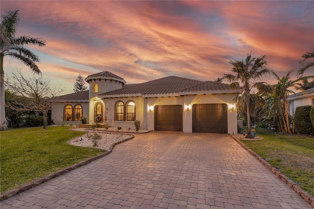 mediterranean / spanish-style home with a front yard, an attached garage, stucco siding, a tiled roof, and decorative driveway