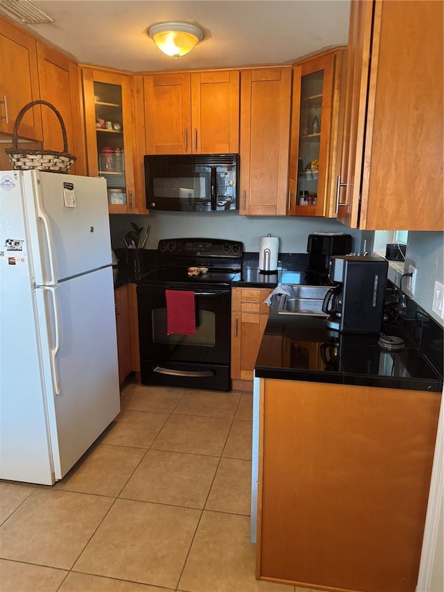 kitchen with brown cabinetry, dark countertops, glass insert cabinets, black appliances, and light tile patterned flooring