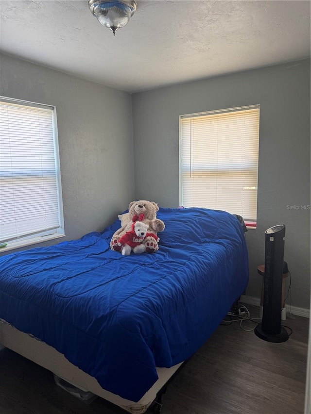 bedroom featuring multiple windows, a textured ceiling, baseboards, and wood finished floors