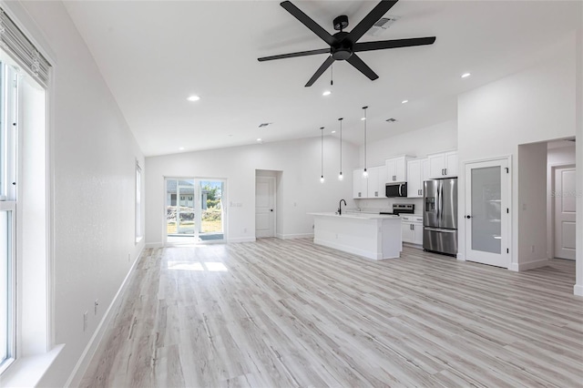 kitchen with white cabinets, appliances with stainless steel finishes, open floor plan, light wood-style floors, and a sink