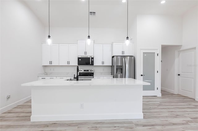 kitchen featuring stainless steel appliances, a sink, an island with sink, and a high ceiling